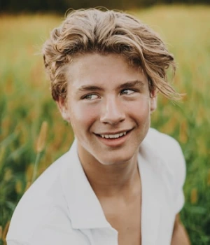 Poetic blonde man standing in an open field, looking charming with a carefree expression.